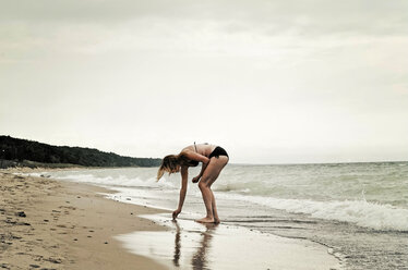 Woman wearing bikini collecting seashells at beach against clear sky - CAVF36978