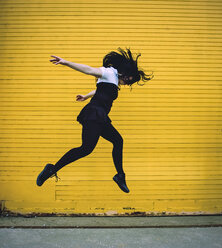 Side view of woman jumping against yellow shutter - CAVF36980