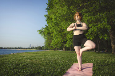 Woman practicing tree pose yoga at park by sea against trees and clear sky - CAVF36983