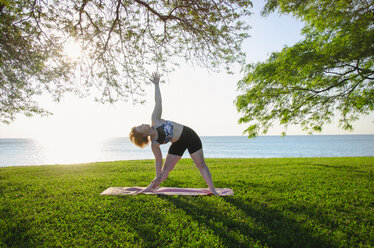 Frau übt Yoga im Park gegen Meer und klaren Himmel - CAVF36984