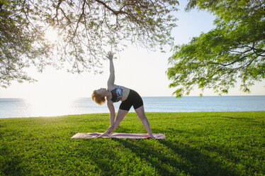 Woman practicing yoga at park against sea and clear sky - CAVF36984