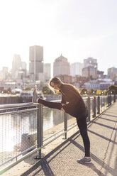 Portrait of happy woman stretching on railing during sunrise - CAVF37026