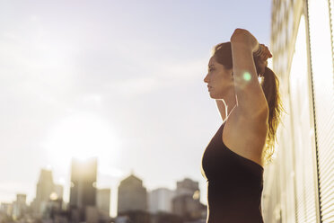 Side view of woman holding hair while standing against sky on sunny day - CAVF37032