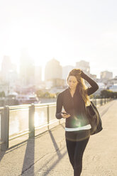 Frau benutzt Smartphone beim Spaziergang in der Stadt an einem sonnigen Tag - CAVF37033