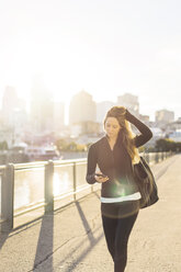 Woman using smart phone while walking in city on sunny day - CAVF37033