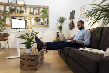 Männlicher Illustrator, der einen Laptop benutzt, während er auf dem Sofa im Kreativbüro sitzt - CAVF37084