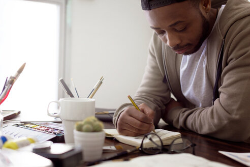 Junger männlicher Illustrator malt am Schreibtisch im Büro - CAVF37097