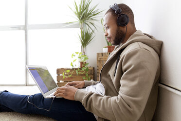 Seitenansicht eines kreativen Geschäftsmannes, der Musik hört, während er einen Laptop im Büro benutzt - CAVF37107