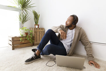 Businessman listening music while sitting on floor at creative office - CAVF37108