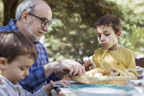 Älterer Mann frühstückt mit Enkeln auf dem Hof - CAVF37124