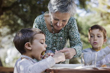 Senior woman feeding breakfast to grandson at yard - CAVF37125