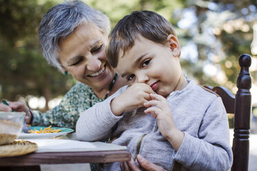 Portrait of cute boy sitting with grandmother at outdoor table - CAVF37130