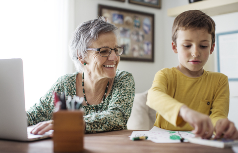 Glückliche ältere Frau betrachtet ihren Enkel, der sich zu Hause Buntstifte aussucht, lizenzfreies Stockfoto