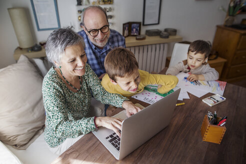 Hochformatige Ansicht von glücklichen Großeltern und Enkeln, die zu Hause einen Laptop benutzen - CAVF37135