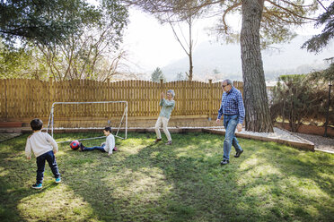 Cheerful grandparents playing soccer with grandsons at yard - CAVF37142