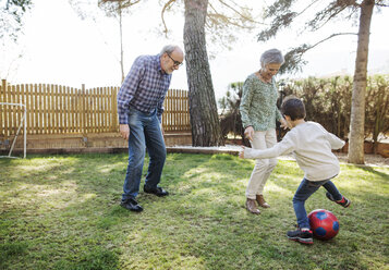 Cheerful grandparents and grandsons playing soccer at yard - CAVF37143