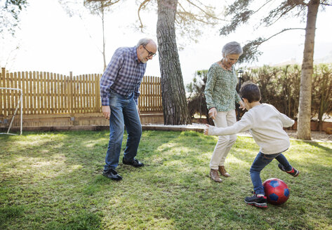 Fröhliche Großeltern und Enkel spielen Fußball im Garten - CAVF37143