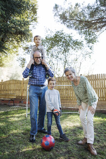 Porträt von glücklichen Großeltern mit Enkeln, die im Garten Fußball spielen - CAVF37145