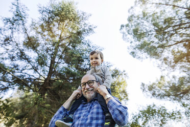 Low angle view of happy senior man carrying grandson on shoulders against sky - CAVF37147