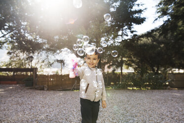 Cheerful boy playing with bubble gun at yard - CAVF37151