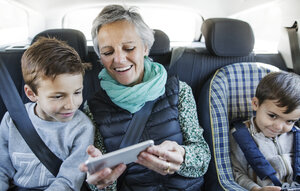 Glückliche ältere Frau benutzt Smartphone mit Enkeln im Auto - CAVF37152