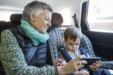 Happy senior woman using smart phone with grandson in car - CAVF37153