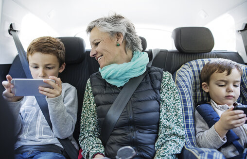 Ältere Frau betrachtet ihren Enkel bei der Benutzung eines Smartphones im Auto - CAVF37155
