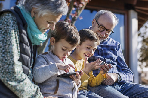 Glückliche Großeltern und Enkel nutzen Smartphones im Park - CAVF37162