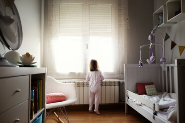 Rückansicht eines Mädchens, das durch ein Fenster im Schlafzimmer schaut - CAVF37169