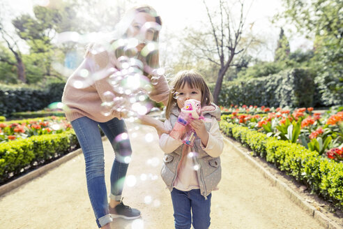 Mother and daughter playing with bubble gun in park - CAVF37176