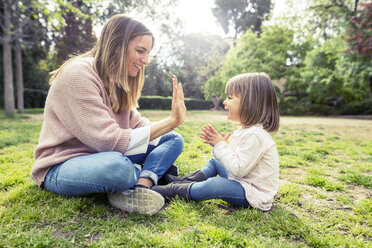 Side view of happy mother and daughter playing patty cake in park - CAVF37178