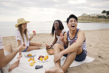 Fröhliche Freunde, die am Strand sitzend Früchte essen - CAVF37199
