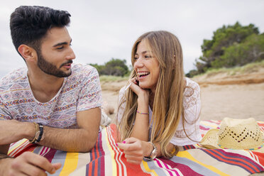 Fröhliches Paar im Gespräch auf einer Decke am Strand liegend - CAVF37201