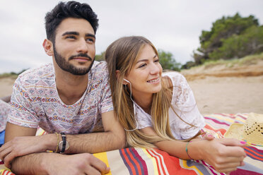 Nachdenkliches Paar, das auf einer Decke am Strand liegt und wegschaut - CAVF37202