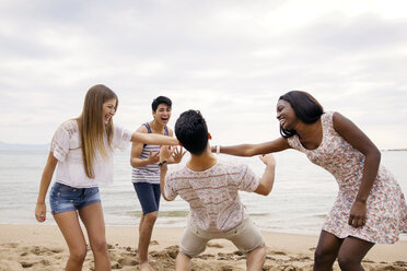 Man passing under women's arms while playing on beach against sky - CAVF37206