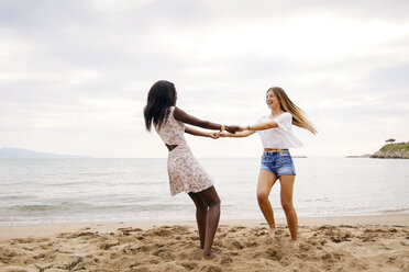 Cheerful female friends playing ring-around-the-rosy on beach - CAVF37207