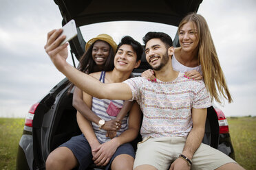 Glückliche multiethnische Freunde machen ein Selfie mit ihrem Smartphone, während sie im Kofferraum eines Autos auf einem Feld sitzen - CAVF37211