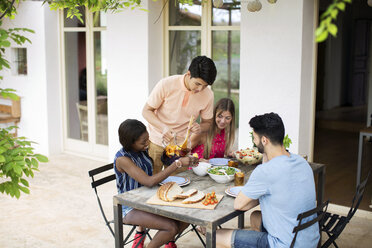 Man serving iced tea to friends at outdoor table - CAVF37216