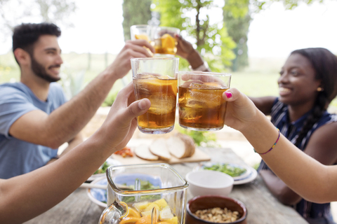 Freunde stoßen mit Eisteegläsern am Tisch im Freien an, lizenzfreies Stockfoto