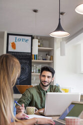 Smiling man looking at woman while using laptop at home - CAVF37231