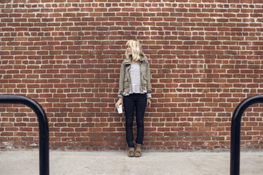 Nachdenkliche Frau, die ein Einwegglas hält, während sie an einer Mauer steht - CAVF37253