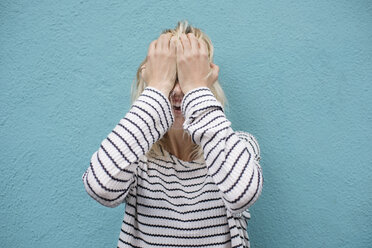 Depressive junge Frau, die ihr Gesicht weiß bedeckt und gegen eine blaue Wand weint - CAVF37258