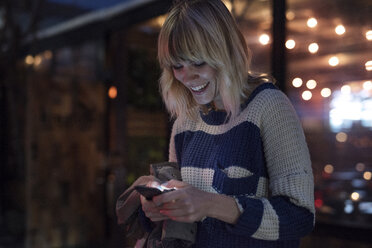 Happy woman using smart phone in illuminated city at night - CAVF37262