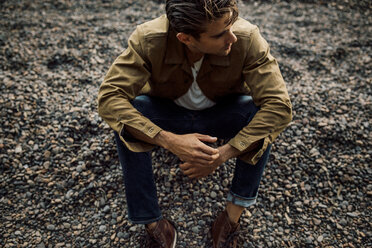 High angle view of thoughtful man looking away while sitting at riverbank during sunset - CAVF37273