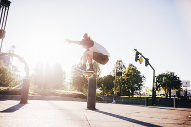 Man performing stunt with skateboard on city street against blue sky during sunny day - CAVF37276