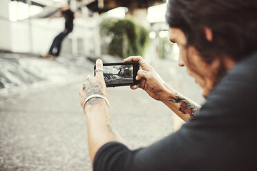 Man photographing with mobile phone on city street - CAVF37278