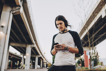 Low angle view of man using mobile phone by bridges against sky in city - CAVF37281