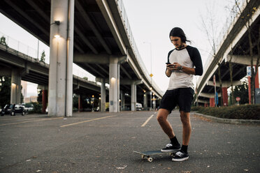 Mann, der ein Mobiltelefon benutzt, während er mit einem Skateboard auf der Straße steht - CAVF37282