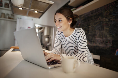 Glückliche Frau arbeitet am Laptop am Tisch - CAVF37283