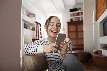 Glückliche Frau schreibt SMS, während sie zu Hause sitzt - CAVF37288